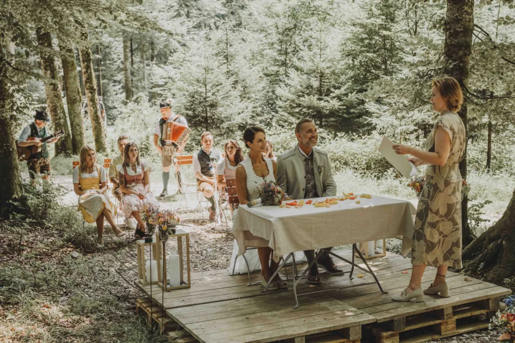 Hochzeit Trauung im Almstadl am Schwarzensee in St. Wolfgang. Die Gäste und das Brautpaar sitzen. Die Standesbeamtin steht vor ihnen.